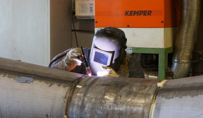 Plasmaschneiden mit mobilem Plasmaschneider: Erstellen eines Lochausschnittes in ein Rohr / Behälter durch einen Facharbeiter mit Schweißhelm